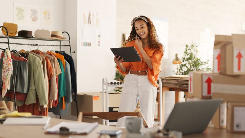 Designer in a vibrant studio using a tablet, surrounded by clothing and packages
