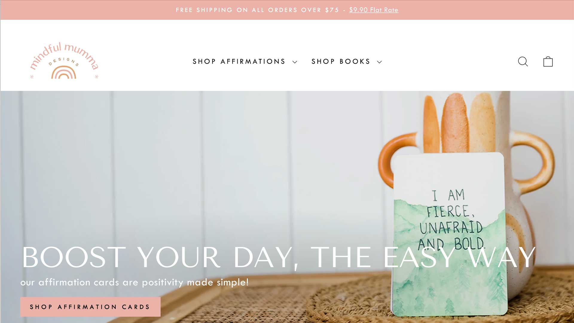 A vase with orange handles props up a card reading I am fierce, unafraid, and bold. Set against a white paneled wall, the elegant website design invites you to BOOST YOUR DAY, THE EASY WAY with options to shop for inspiring affirmations and books.